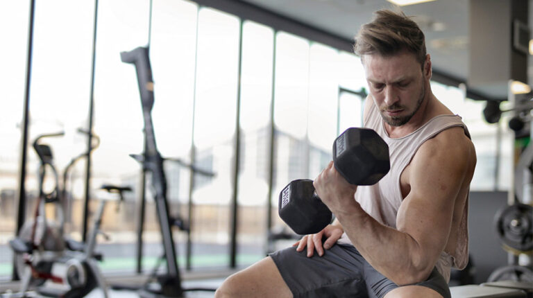 man-in-white-tank-top-and-grey-shorts-lifting-dumbbell-Metabolic-Benefits-of-Exercise-How-Building-Muscle-Can-Help-You-Burn-More-Calories